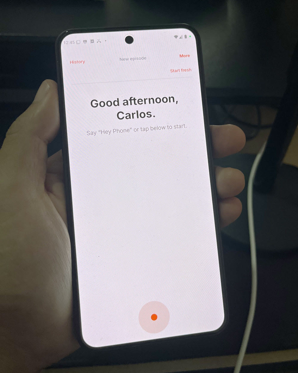 The phone.md home screen on a Nothing Phone 3, held in one hand. It reads “Good afternoon, Carlos.” above “Say ‘Hey Phone’ or tap below to start.”, with an orange listening circle at the bottom of the screen.